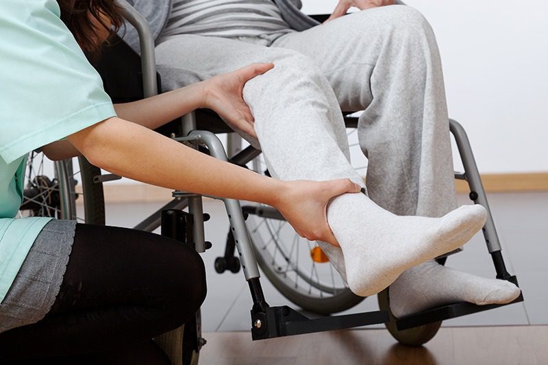 A young physiotherapist exercising the leg of a wheelchair patient.