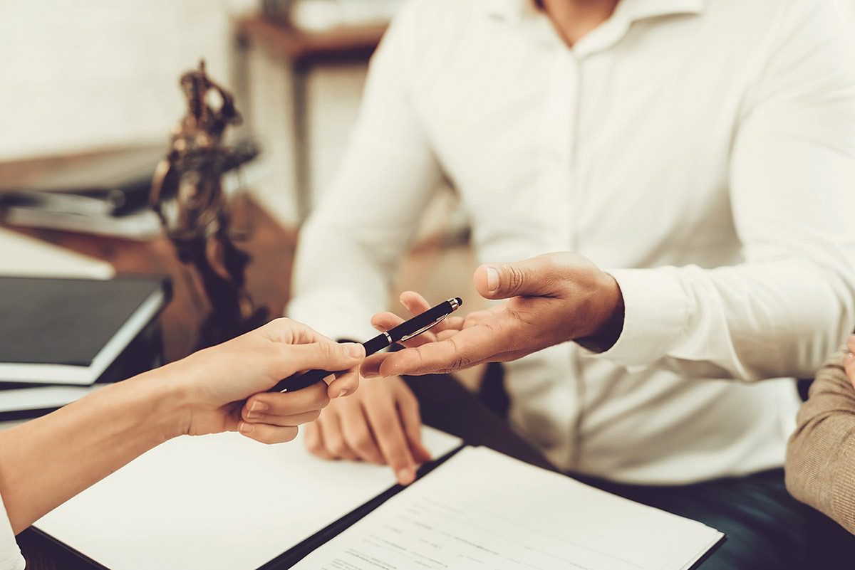 An image of one person being handed a pen to officiate or sign a settlement agreement.