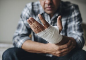 An image of a man holding his arm while staring at his hand wrapped in gauze despondently.