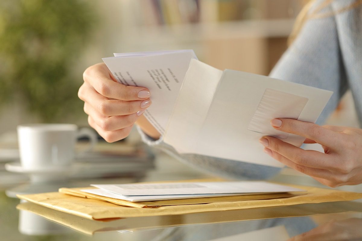 A woman's hands opening a series of letters from the mail.