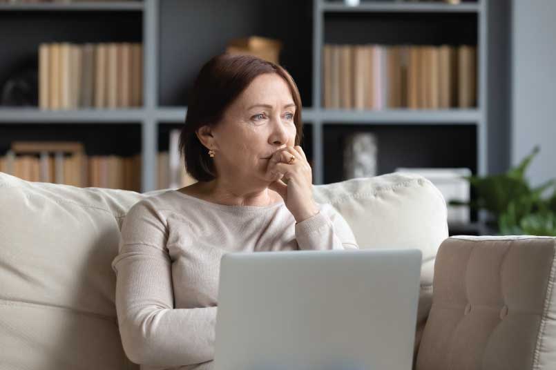 A woman staring pensively out her window after using her laptop.