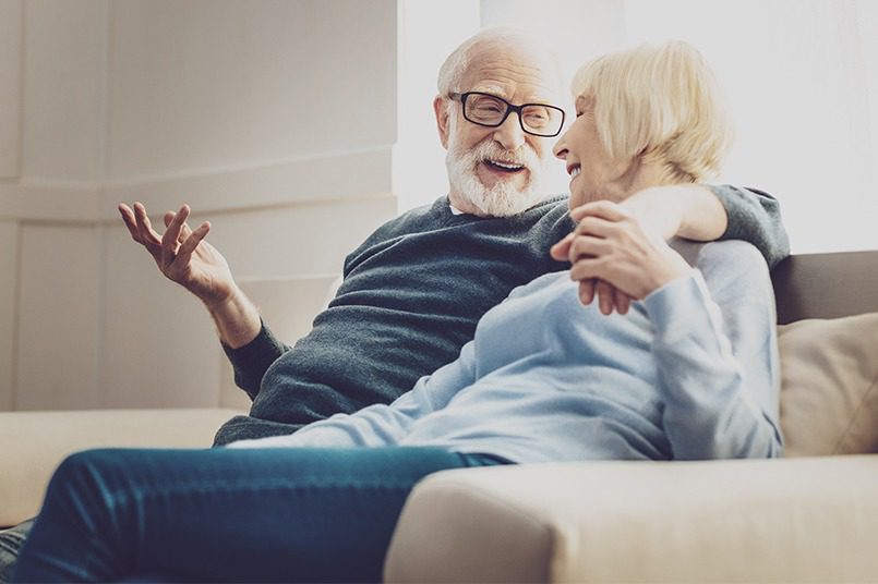 An elderly couple chatting while snuggling on their home couch.